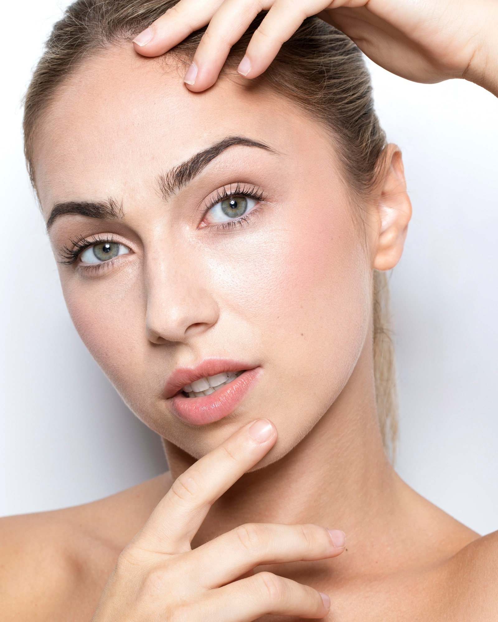 Beauty portrait of a young woman with green eyes touching her forehead and chin against a white background