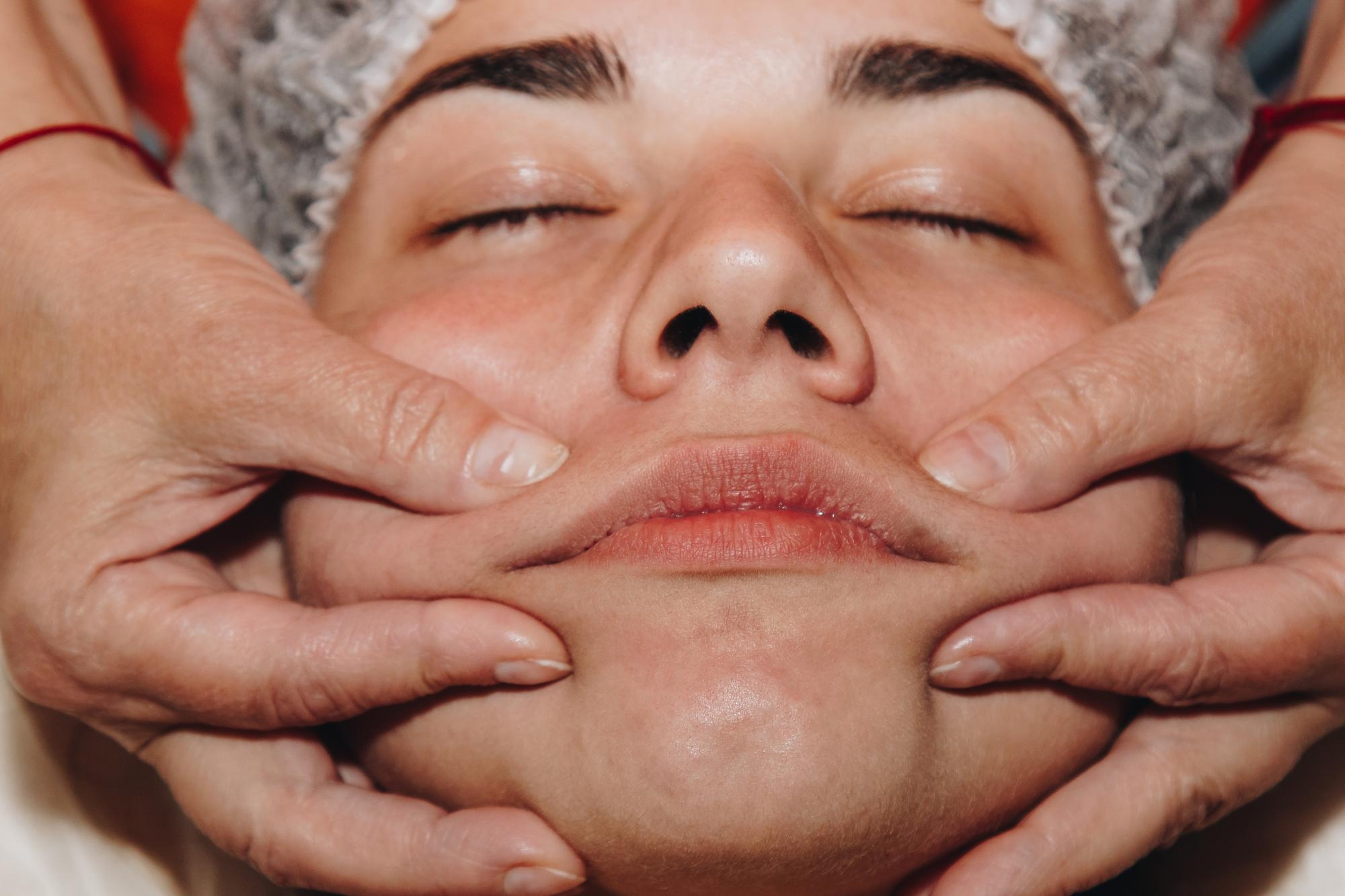 Close-up of a woman receiving a facial massage as a therapist's hands work along her jaw and cheeks