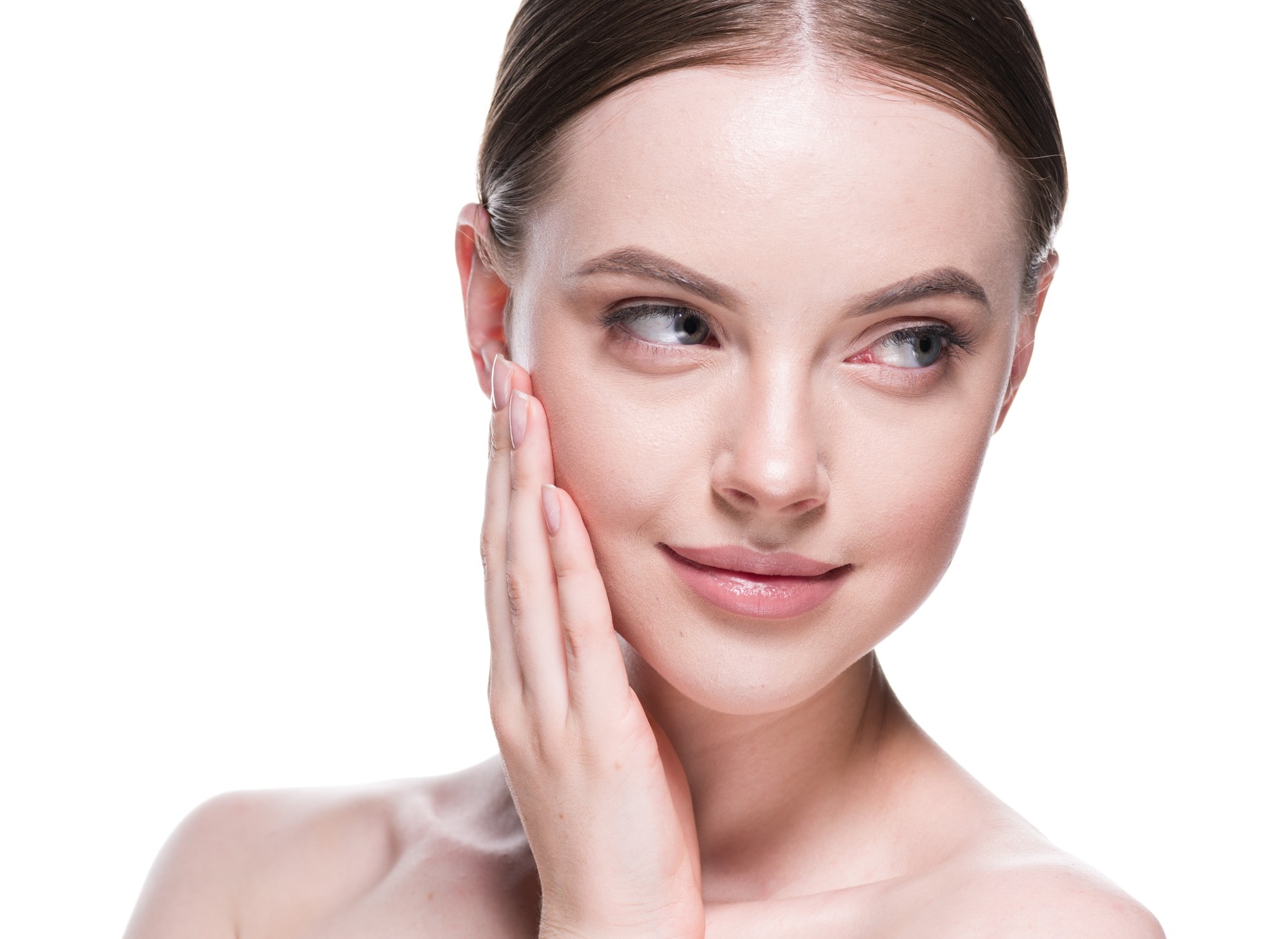 Smiling woman with clear, natural skin touching her cheek and looking to the side against a white background