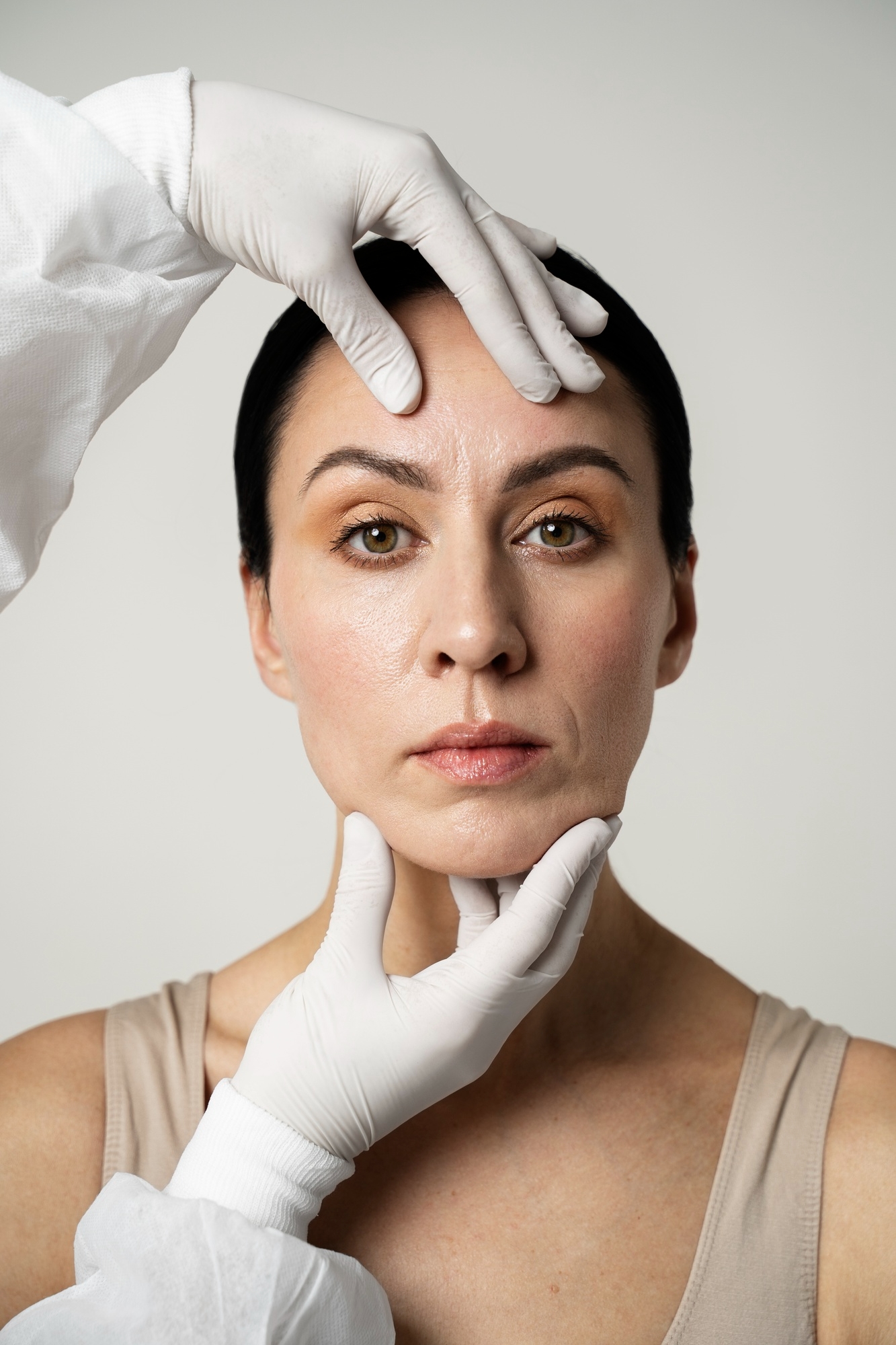 Practitioner in white gloves assessing the face of a dark-haired woman during a cosmetic consultation