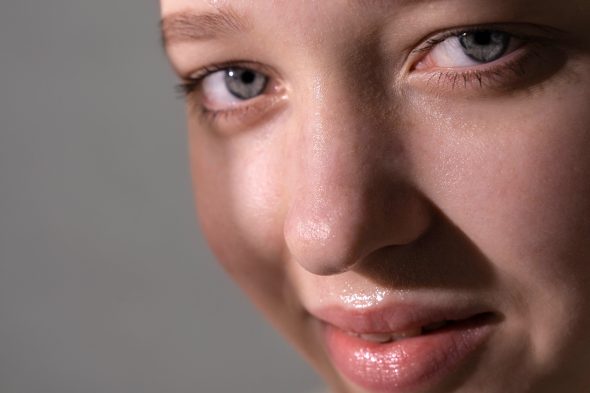 Close-up of a woman's face with glowing, healthy skin and blue eyes against a grey background