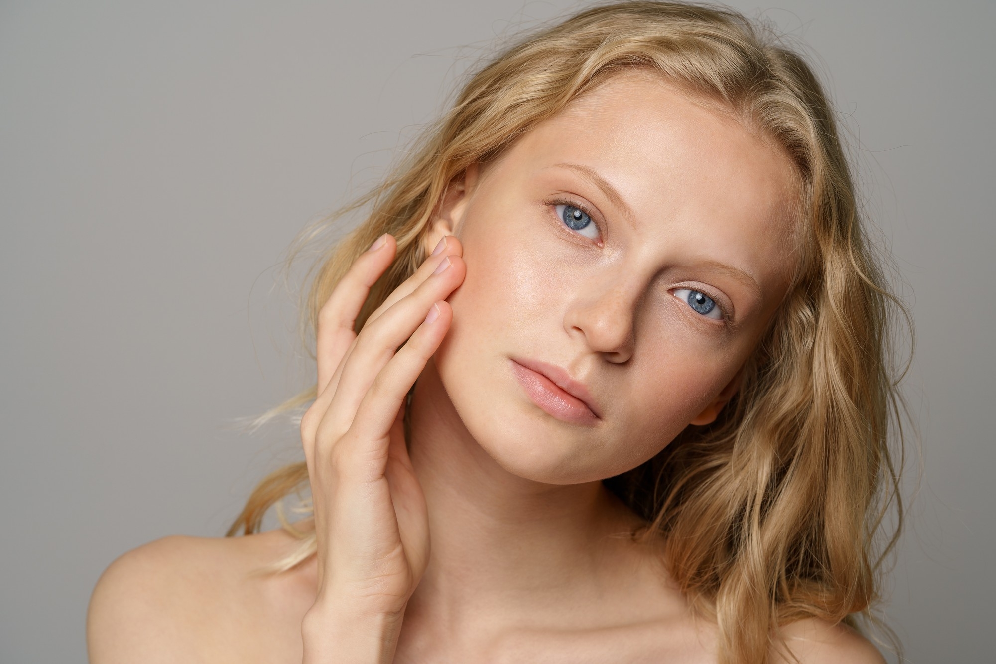 Close-up of a woman gently touching her cheek with clear, healthy-looking skin.