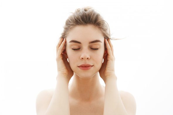 Woman with her eyes closed resting her fingertips on her temples against a bright white background